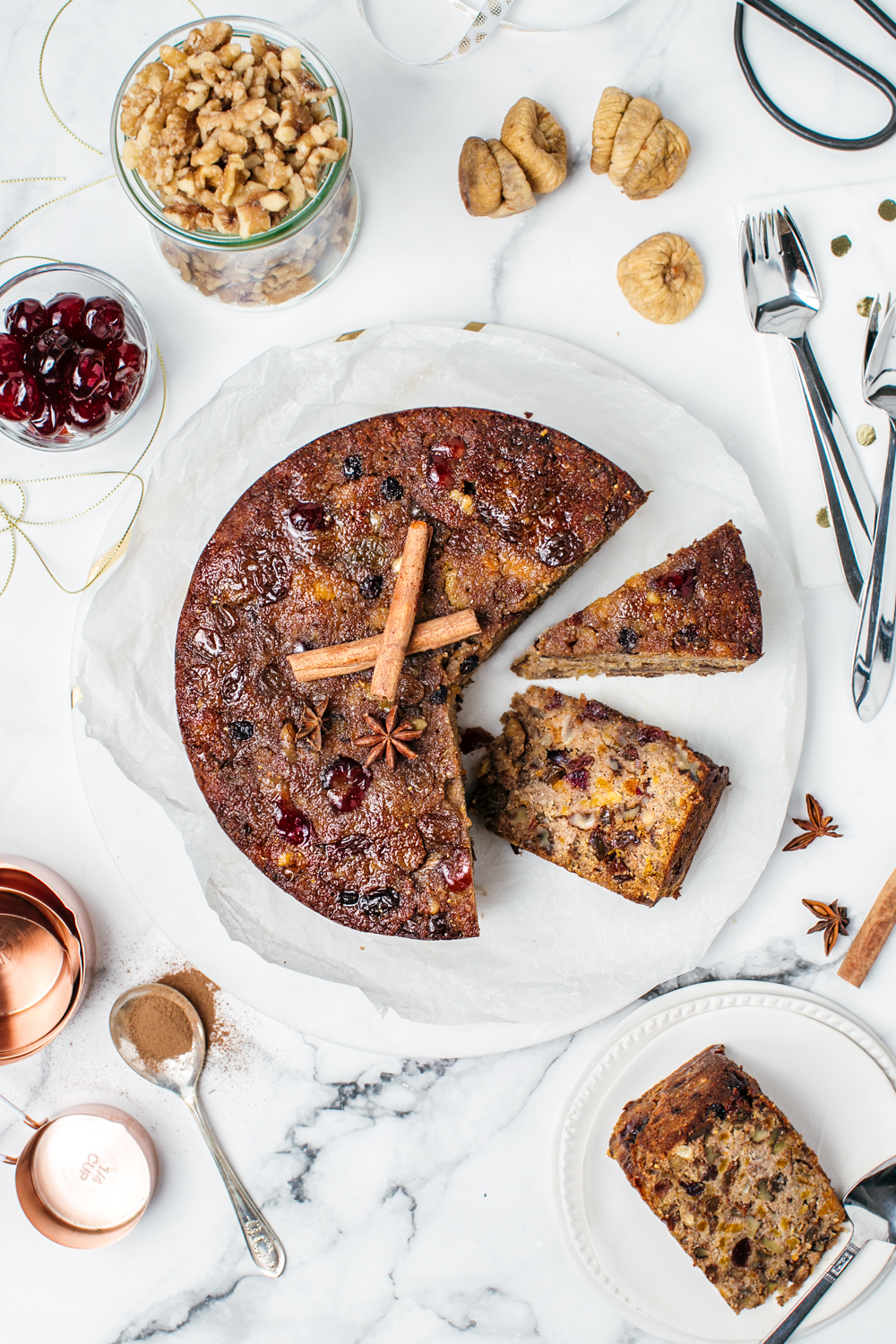 Flatlay of healthy Christmas fruit cake sliced and surrounded with nuts, cranberries and cutlery