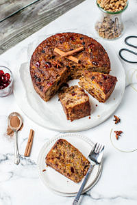 Christmas fruit cake on a white plate partly sliced, one slice on a side plate with fork