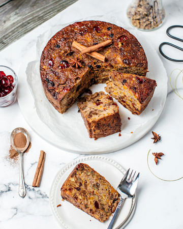 Christmas fruit cake on a white plate partly sliced, one slice on a side plate with fork