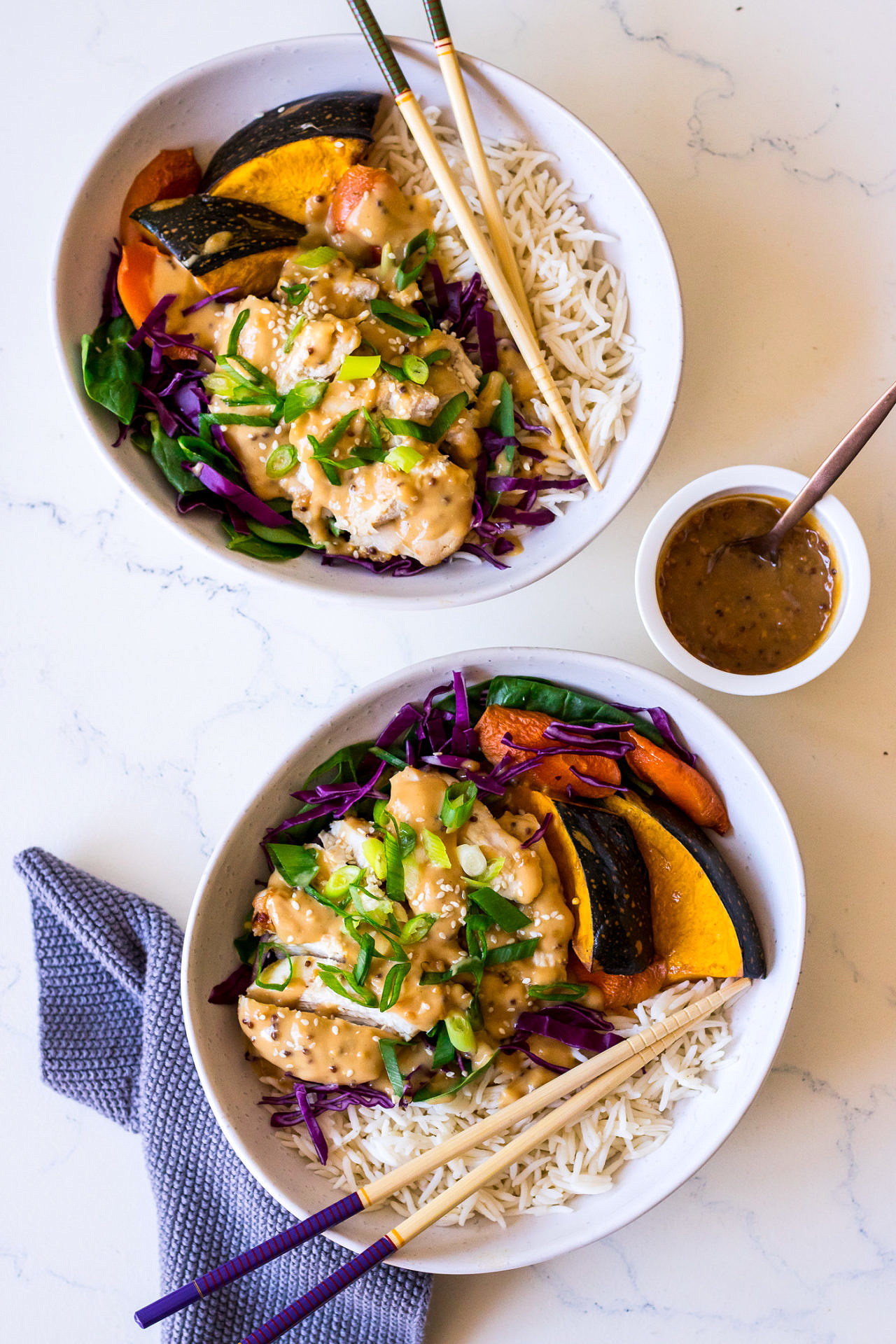 Two irregular white ceramic bowls with rice, roasted vegetables, purple cabbage, chicken and miso mustard dressing