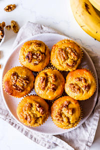 Pumpkin banana and walnut muffins arranged on small white ceramic plate, on top of neutral linen napkin