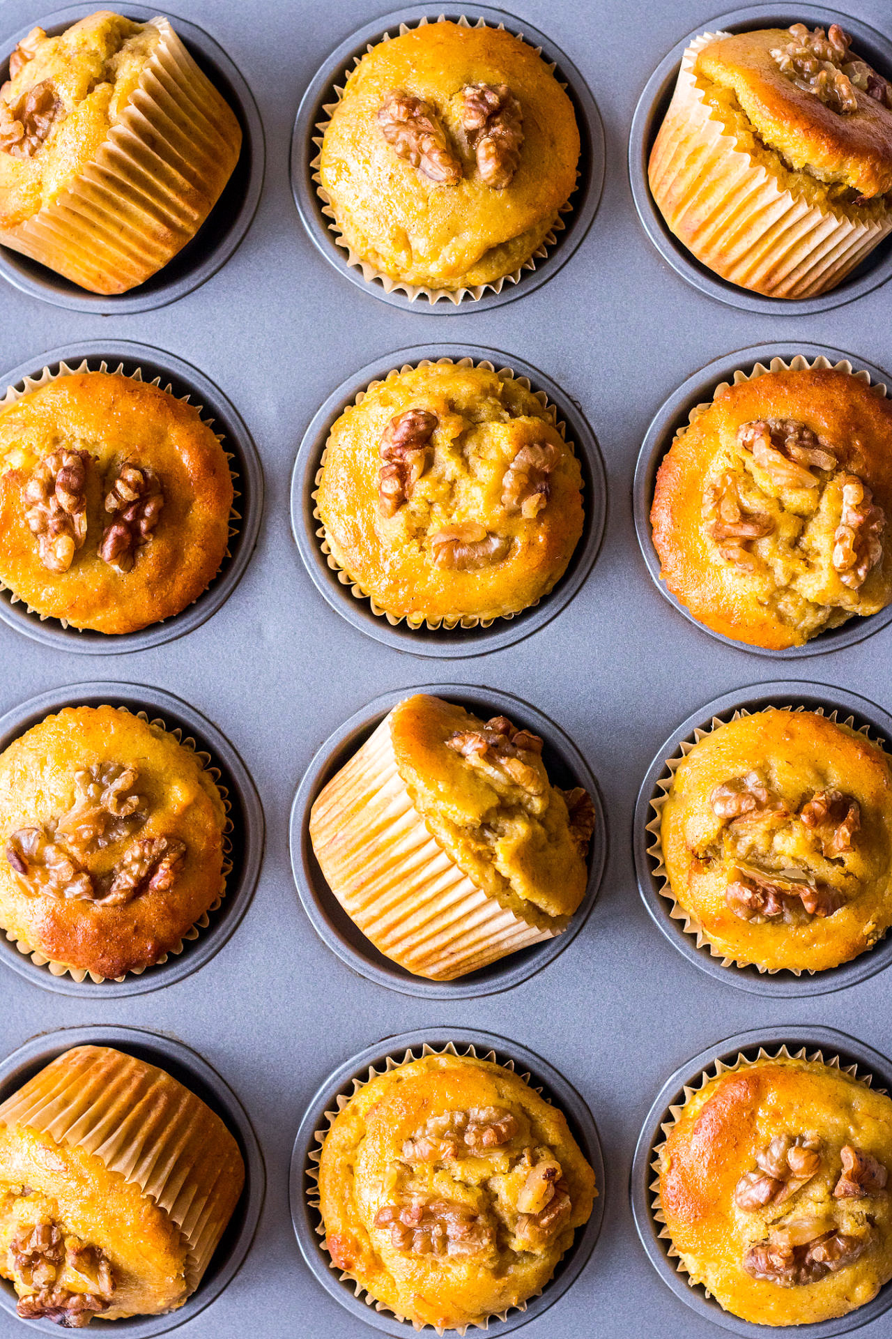 Dark metal muffin tray filled with healthy pumpkin, banana and walnut muffins