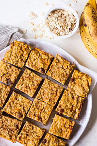 Banana oatmeal bars on a white plate with rolled oats and bananas