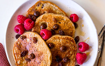 Vegan protein pancakes on white ceramic plate with chocolate chips, raspberries and maple syrup