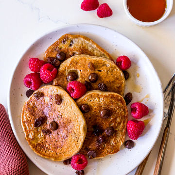 Vegan protein pancakes on white ceramic plate with chocolate chips, raspberries and maple syrup