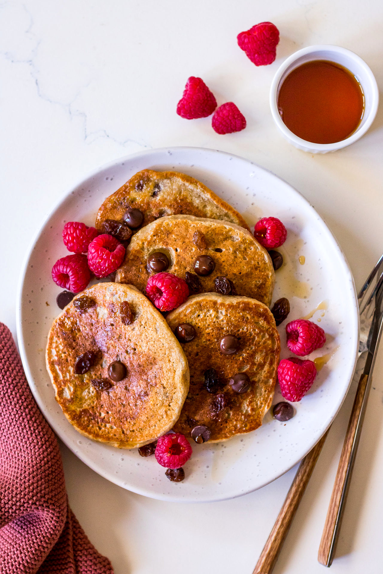 Top view of protein pancakes with raspberries, chocolate chips and maple syrup on a white plate