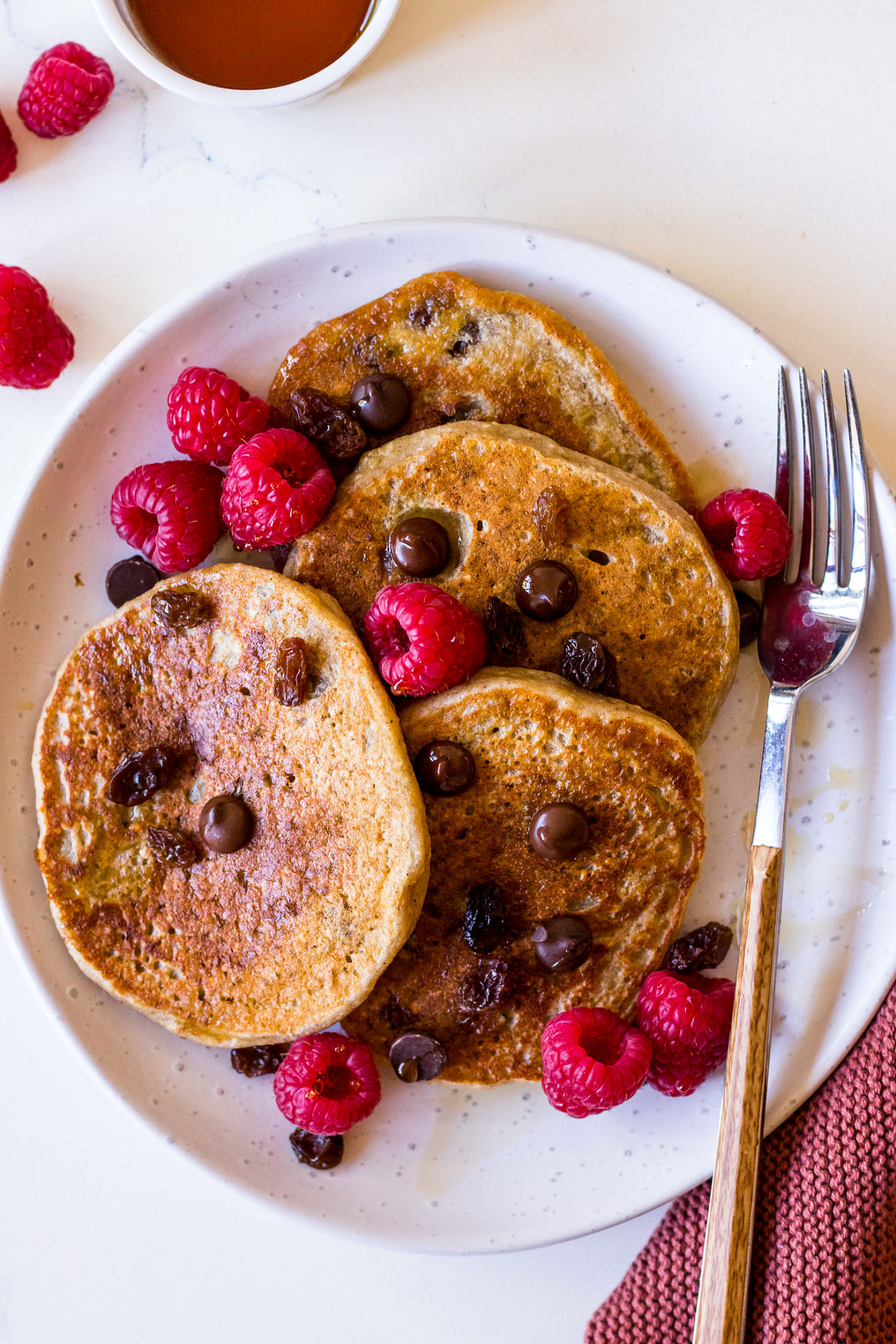 Vegan vanilla protein pancakes topped with raspberries and chocolate chips on a white plate