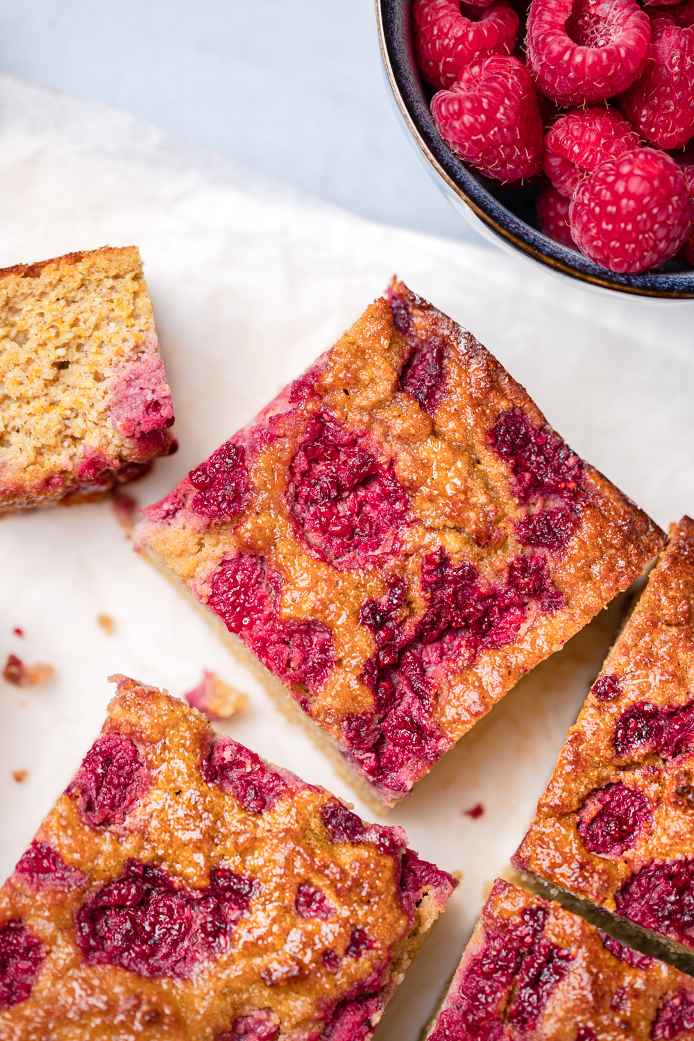 Close up squares of orange almond cake topped with raspberries
