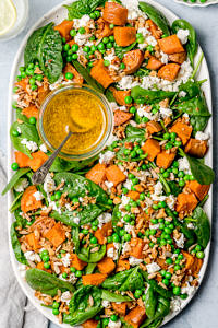 Salad of baby spinach, sweet potato and peas topped with feta, seeds and mustard dressing