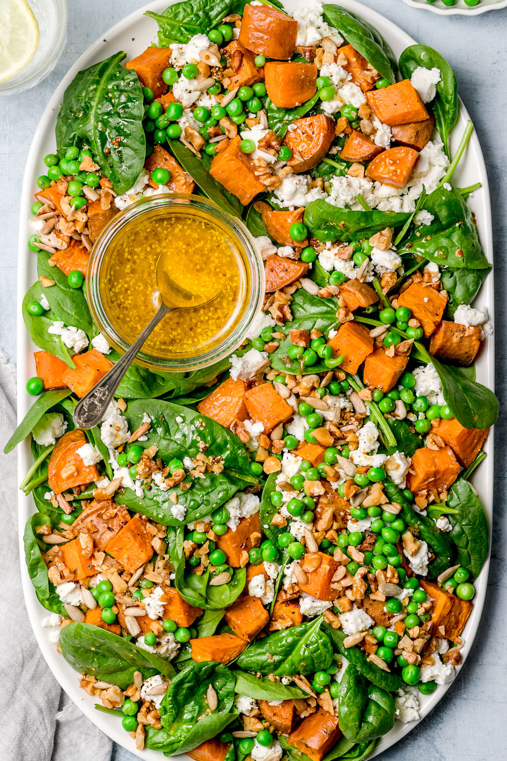 salad of spinach, sweet potato, peas and feta topped with mustard dressing in small bowl