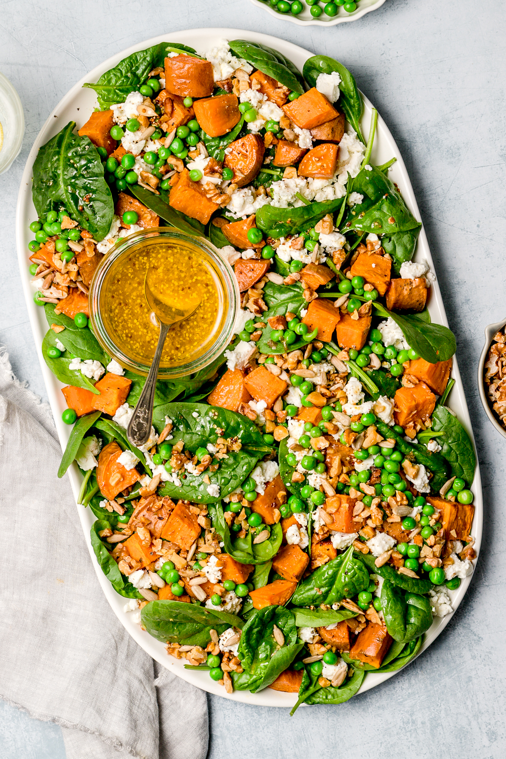 spinach, sweet potato, pea and feta salad on oval ceramic plate, small dish of salad dressing