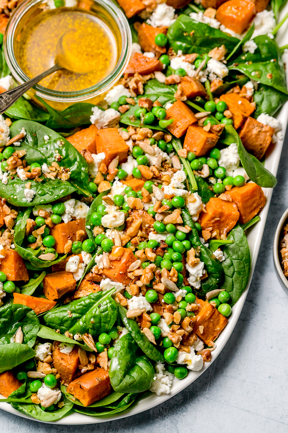 baby spinach, sweet potato, pea and feta salad with nuts and seeds, oval ceramic plate