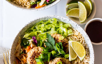 Speckled bowls with brown rice, pork patties, salad, herbs and lime
