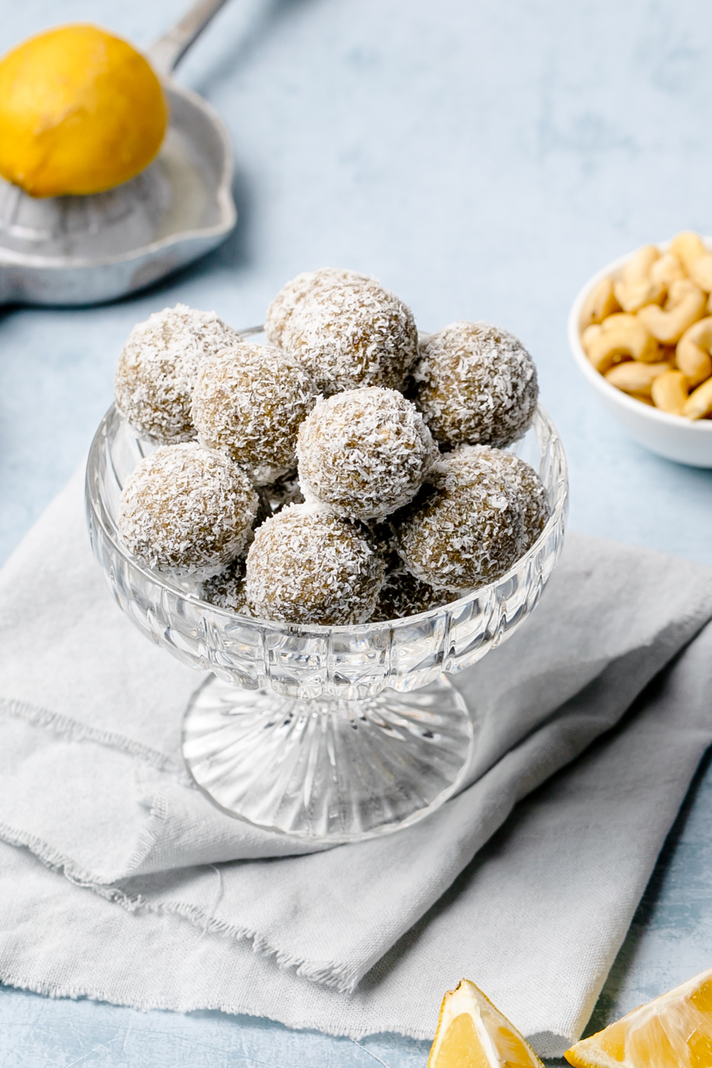 lemon, cashew and coconut energy balls in a small glass bowl, blue table background