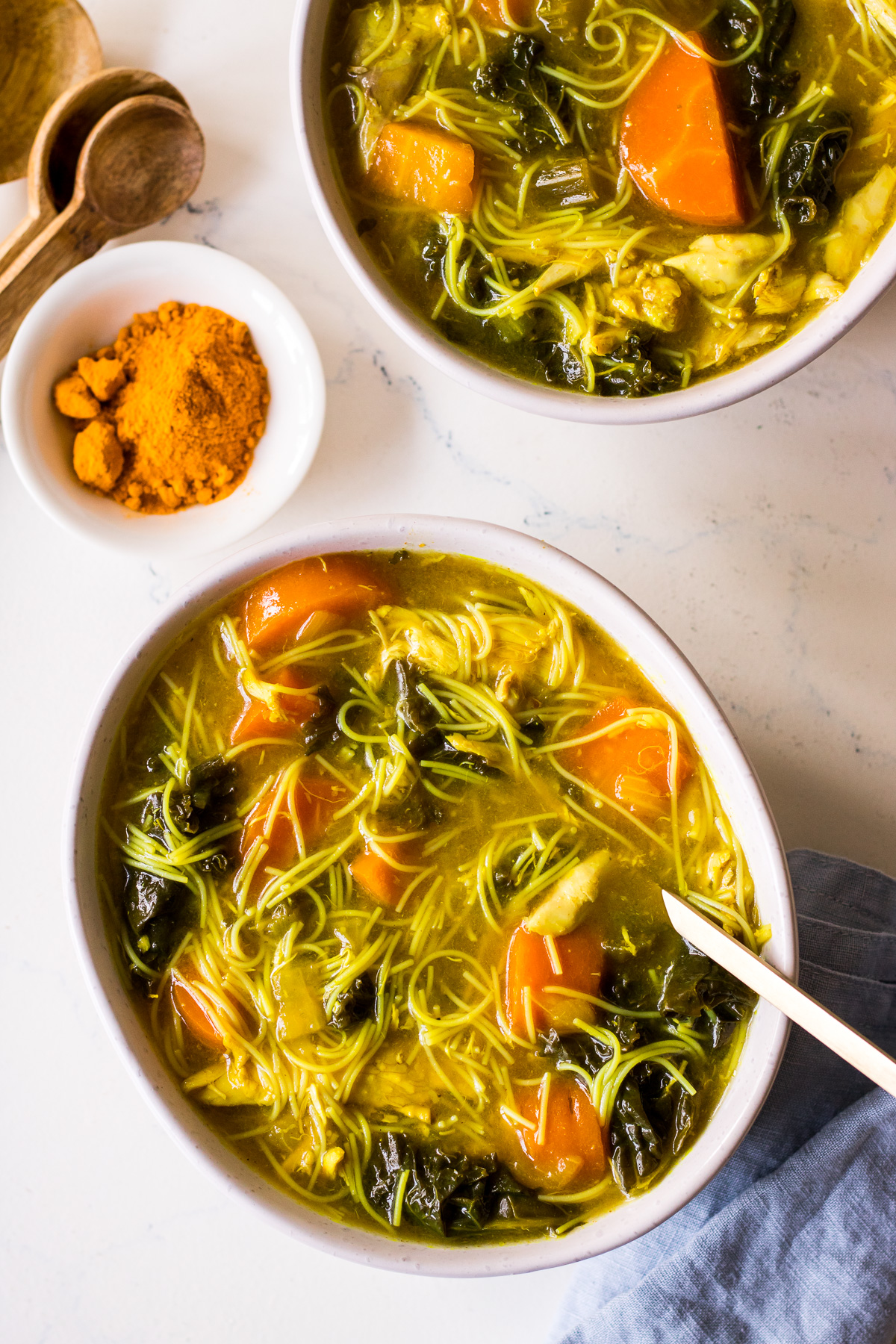 Bowl of chicken noodle soup with turmeric, kale and carrots, blue napkin to the side