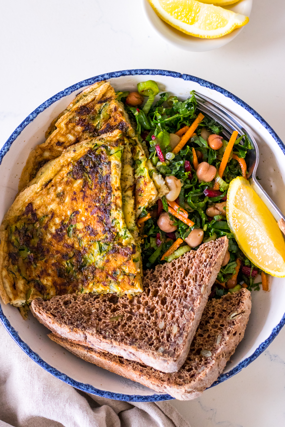 Zucchini herb omelette sliced in a bowl with brown toast and kale salad