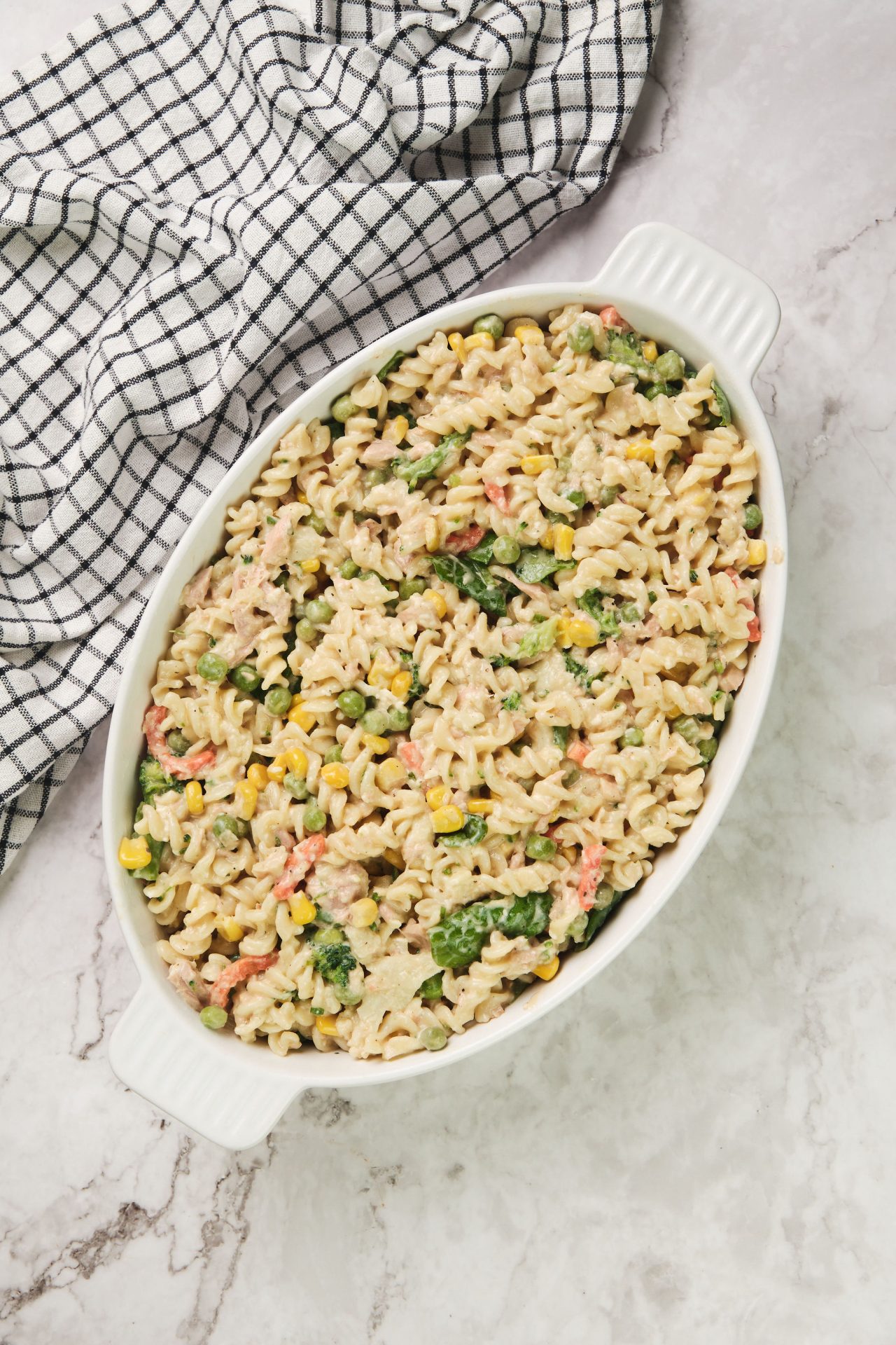 Tuna, vegetables, spiral pasta and white sauce arranged in a baking dish for creamy tuna pasta bake