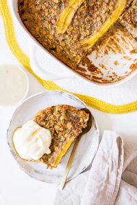 Baked oats in a square white baking dish with banana on top, and a side plate of baked oats with yoghurt