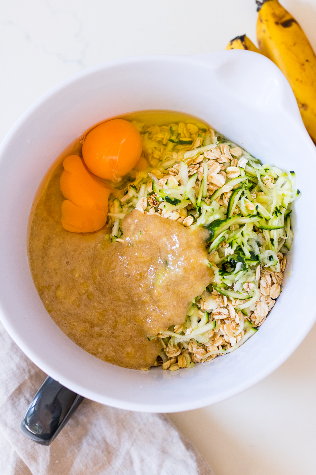 Mixing bowl with grated zucchini, oats, mashed banana, eggs