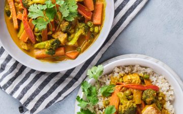 Vegetable yellow curry with tempeh strips served in bowls with brown rice