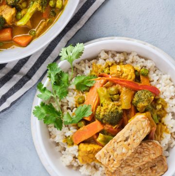 Vegetable yellow curry with brown rice and tempeh strips in a bowl