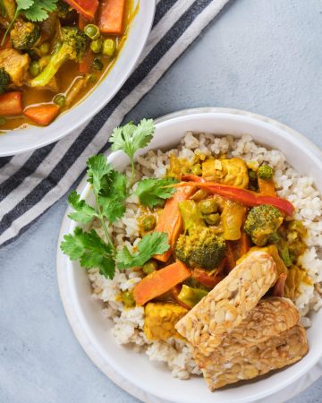 Vegetable yellow curry with brown rice and tempeh strips in a bowl