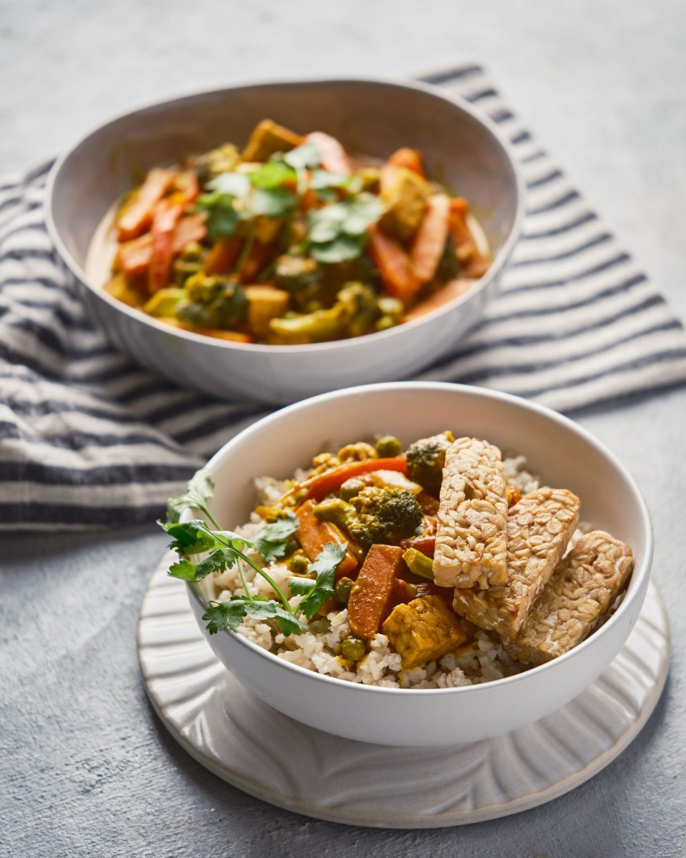 Bowl of yellow curry with vegetables, brown rice and tempeh
