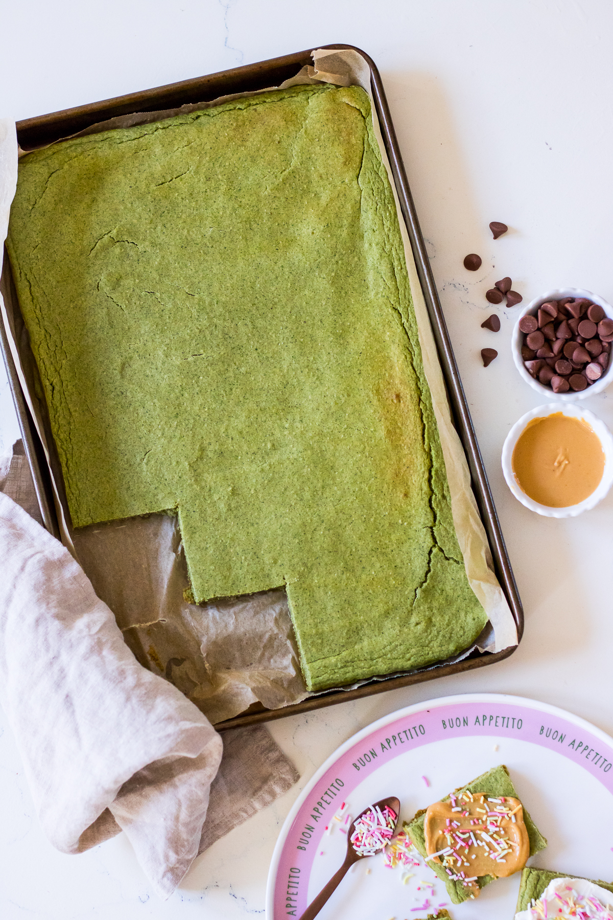 Image of green pancakes baked into a large sheet pan, some cut into square shape with peanut butter and sprinkles