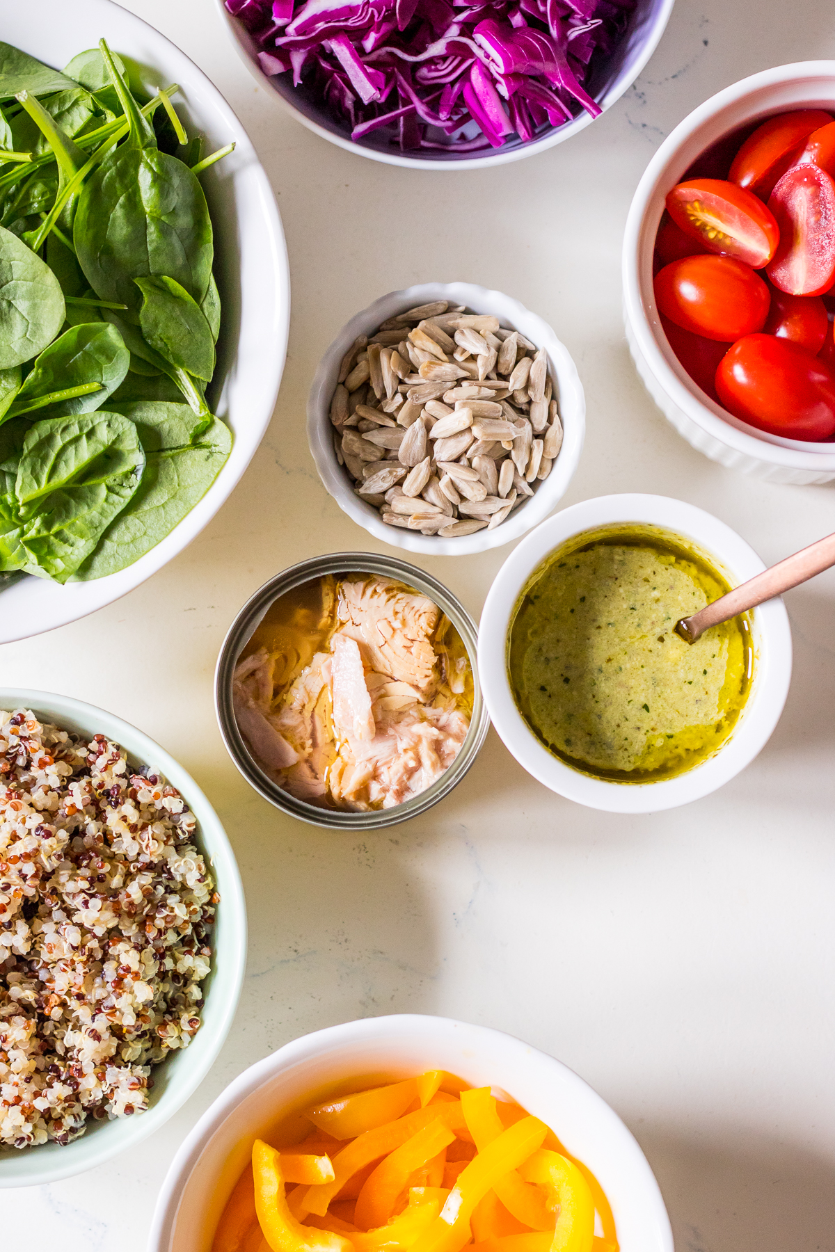Ingredients to make a tuna quinoa salad arranged into individual bowls including spinach, capsicum, cabbage and tomatoes