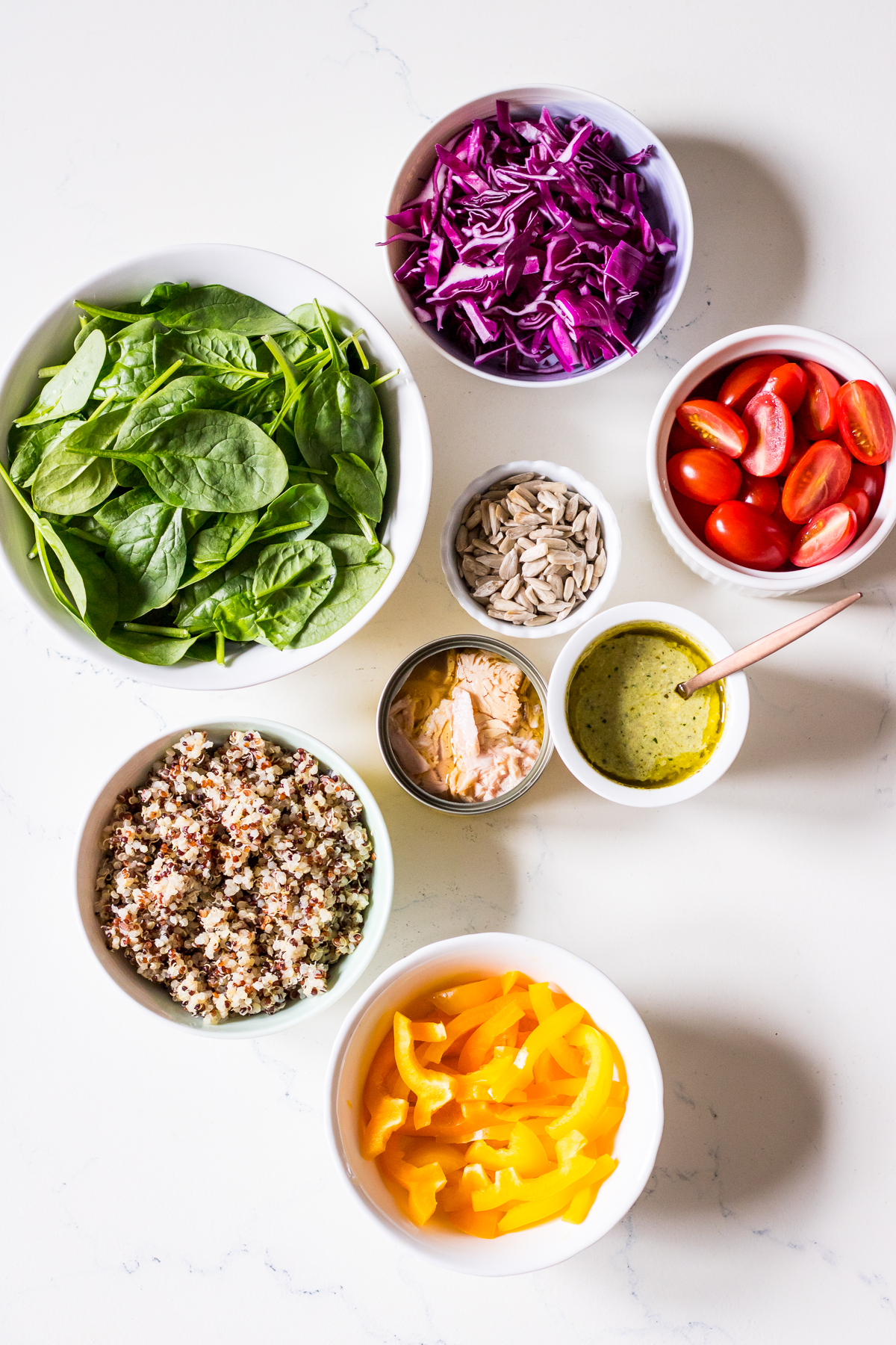 An image of ingredients for a salad arranged in individual bowls including vegetables, quinoa, tuna, seeds and pesto
