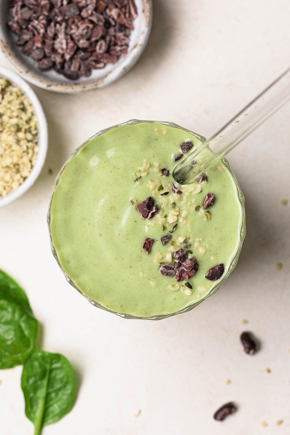 Top down image of a banana avocado green smoothie in a glass topped with cacao nibs