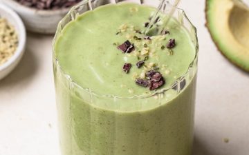 Avocado, banana and spinach green smoothie in a clear glass with a glass straw