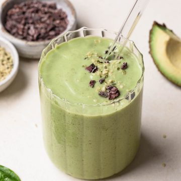 Avocado, banana and spinach green smoothie in a clear glass with a glass straw