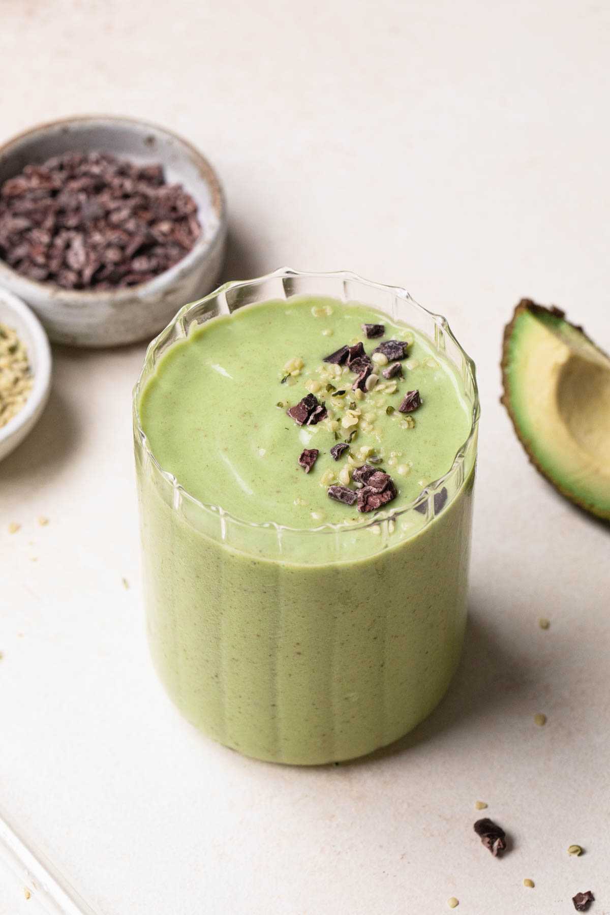 Image of an avocado banana green smoothie in a clear glass with cacao nibs