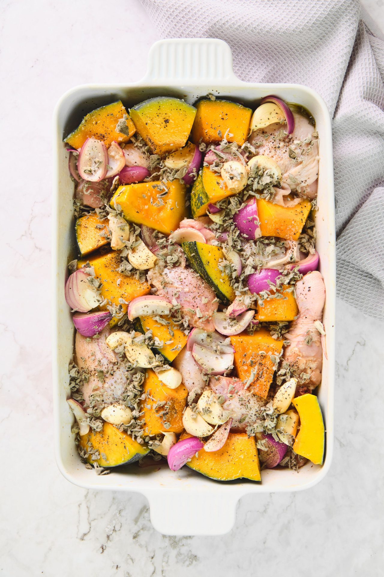 White baking dish with chicken, pumpkin, onion and herbs