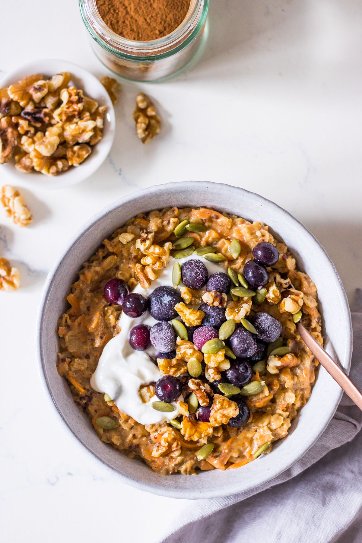 Carrot cake porridge in a small bowl with yoghurt, blueberries, nuts and seeds on top