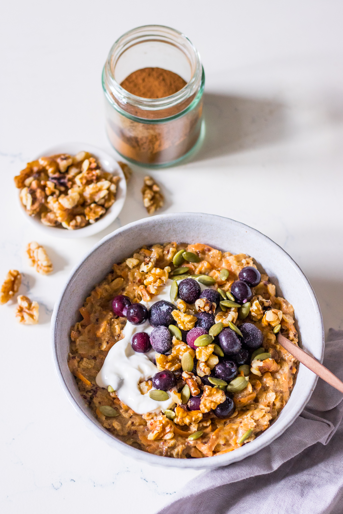 A bowl of carrot oatmeal with berries and walnuts, with walnuts scattered around the bowl