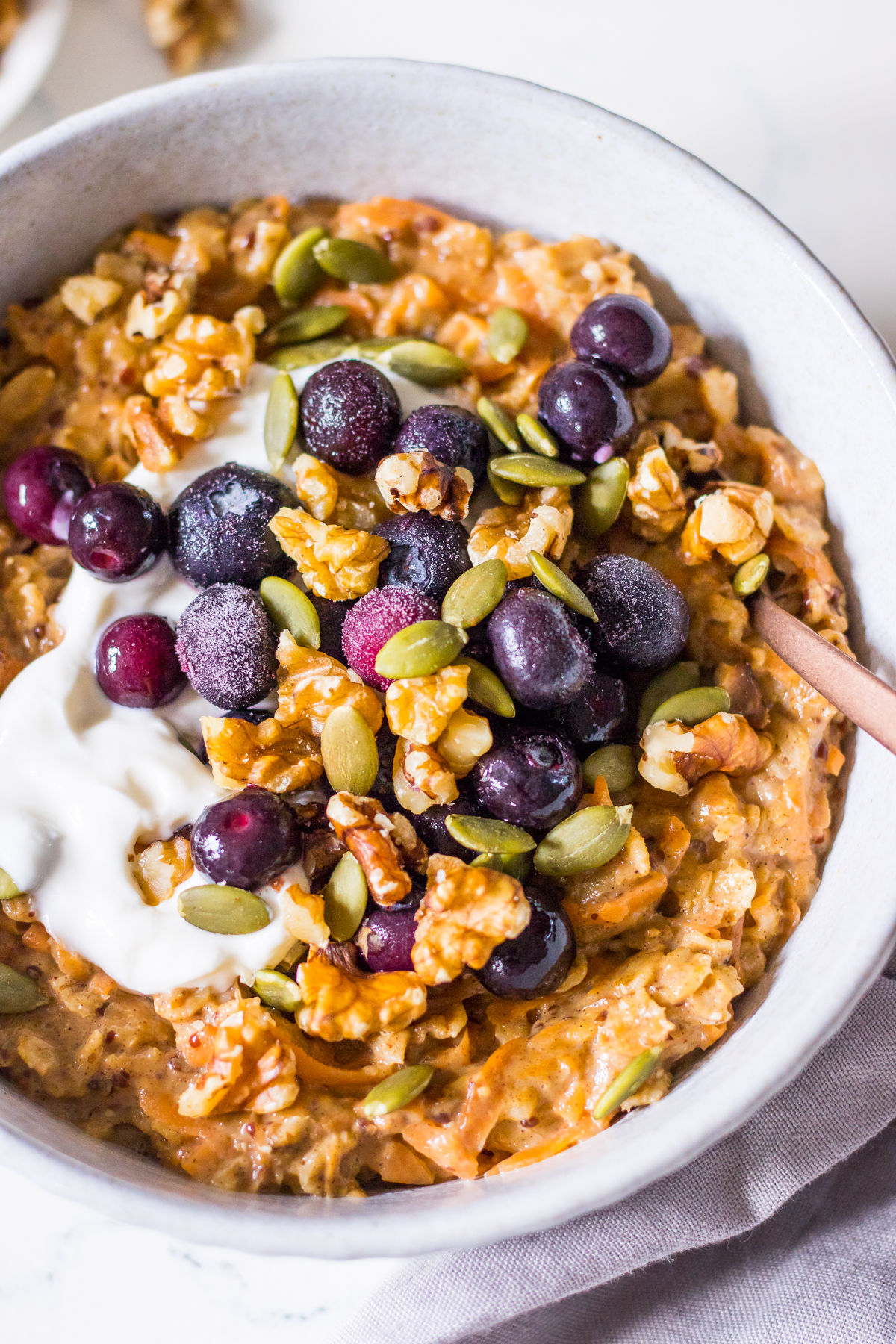 Close up image of a bowl of carrot cake porridge with yoghurt, blueberries and nuts