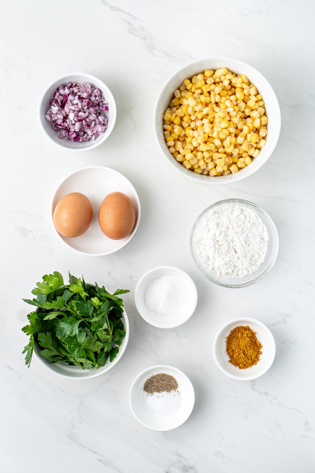 Image of ingredients needed for healthy gluten free corn fritters; eggs, corn, herbs, spices, red onion.