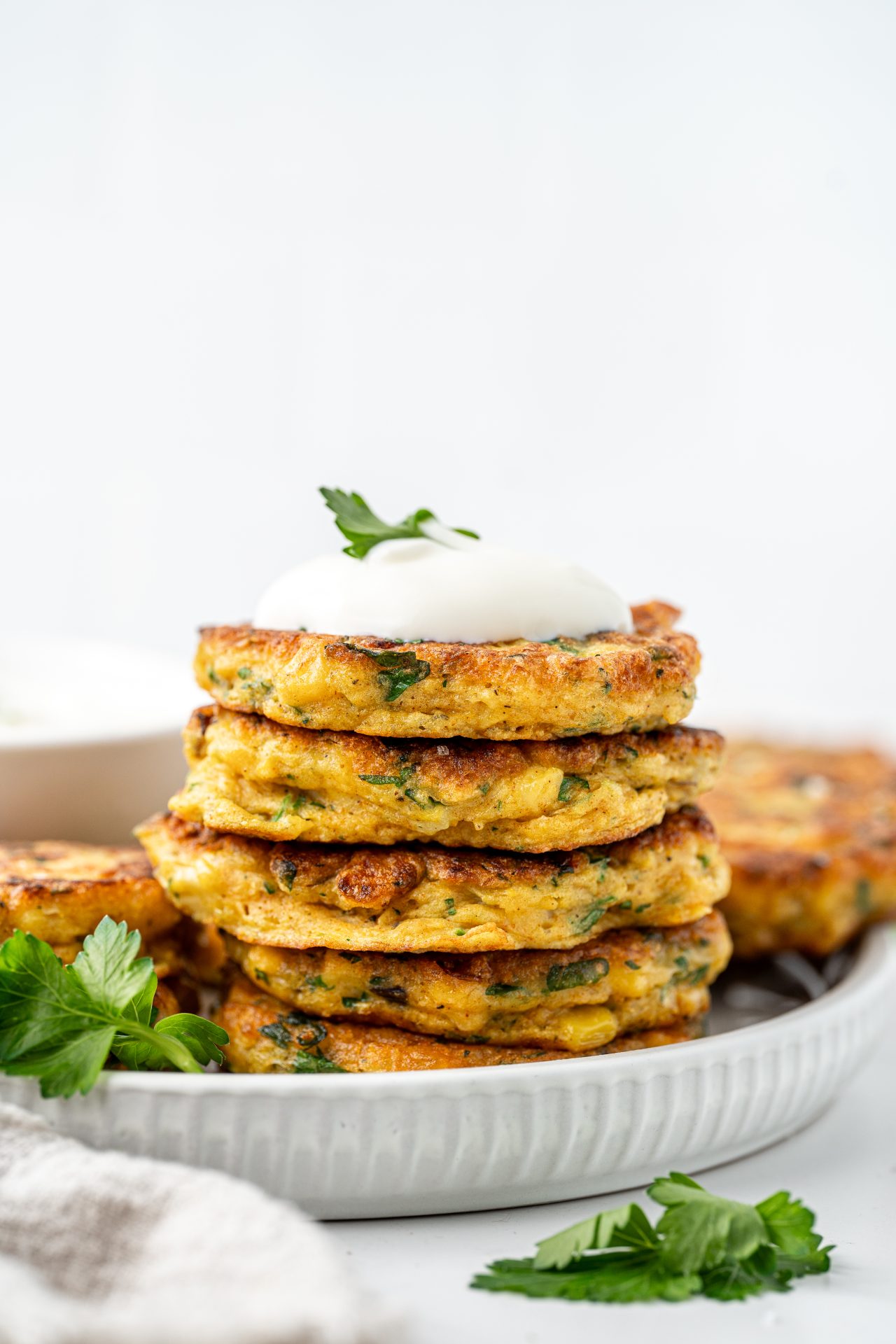 Side view of a stack of homemade easy gluten free corn fritters with a dollop of Greek yoghurt and fresh parsley.