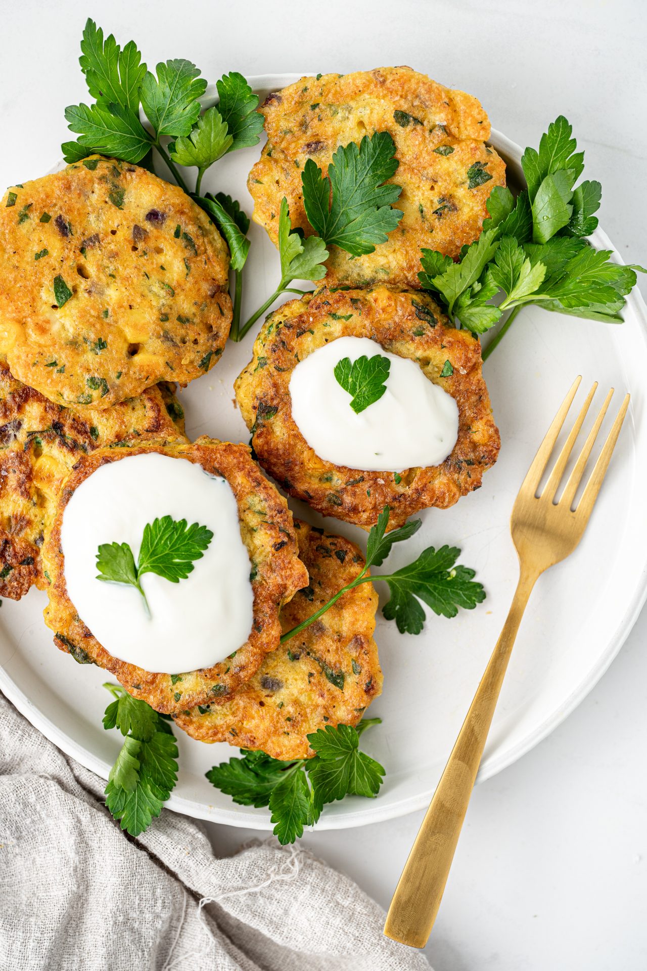 A plate of easy gluten free corn fritters, homemade, with Greek yoghurt sauce and fresh parsley.