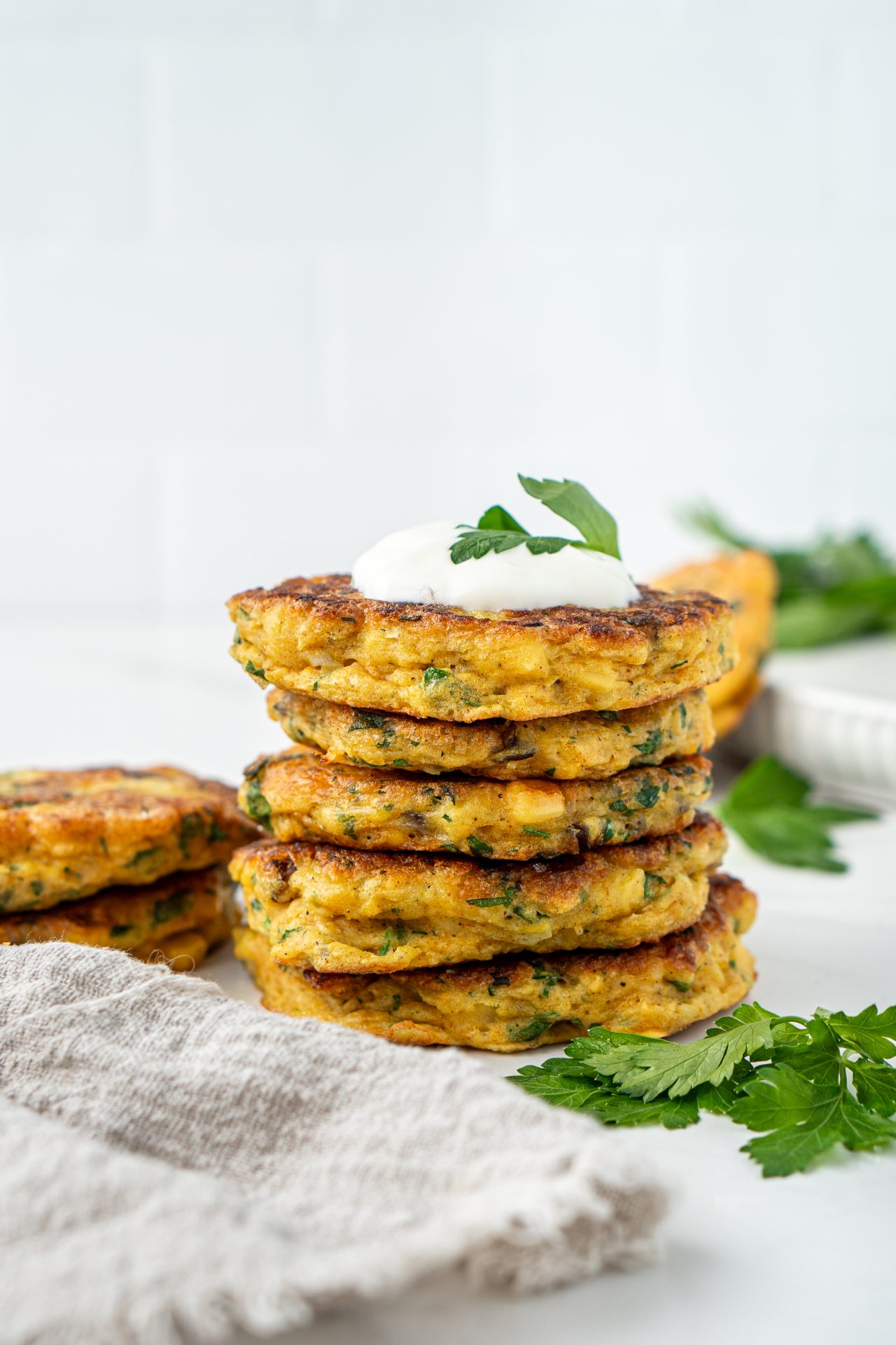 Stack of healthy homemade gluten free corn fritters topped with Greek yoghurt and fresh green herbs.