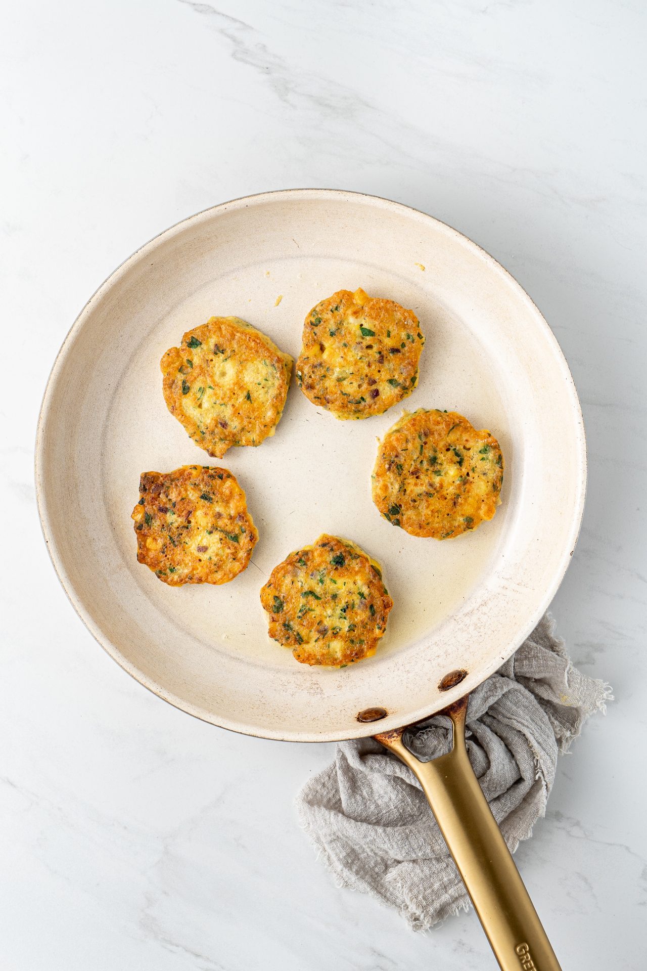 Image of corn fritters cooking in a white ceramic frying pan.