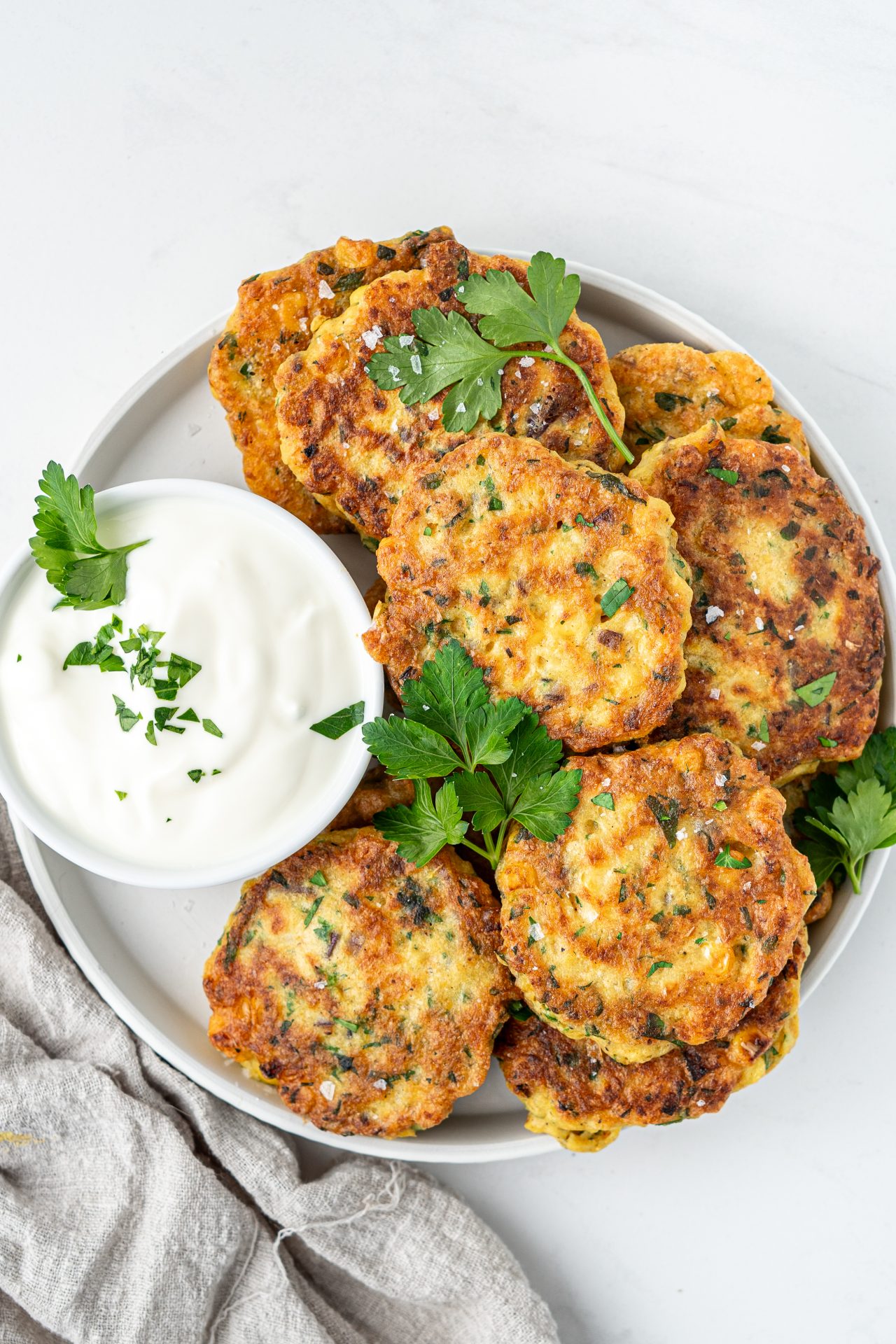 Top down view of a plate of easy homemade gluten free corn fritters with a yoghurt sauce and herbs.