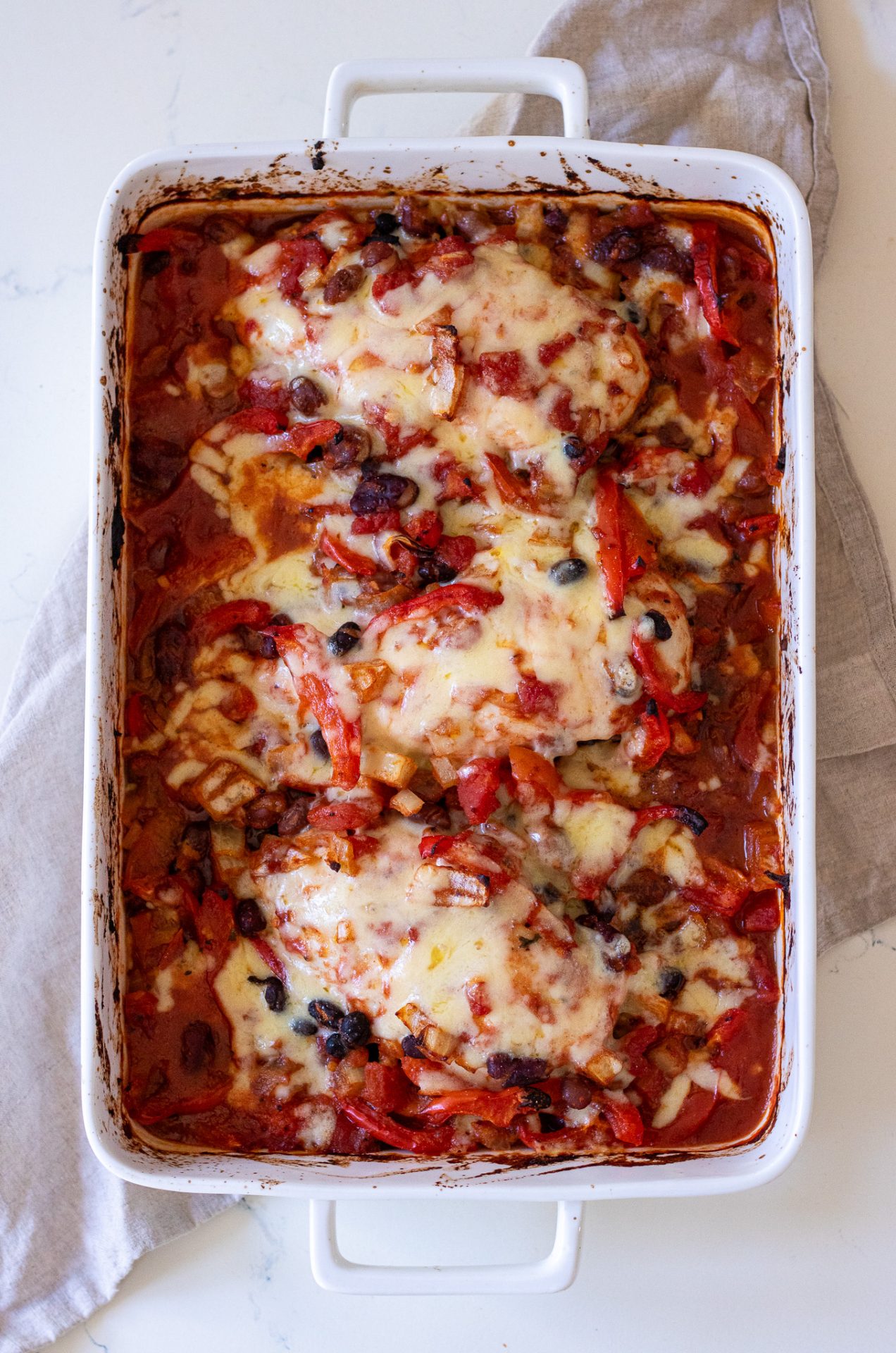 Top view of Healthy Chicken Taco Bake in a white baking dish; capsicum, bean mix and melted cheese on the top