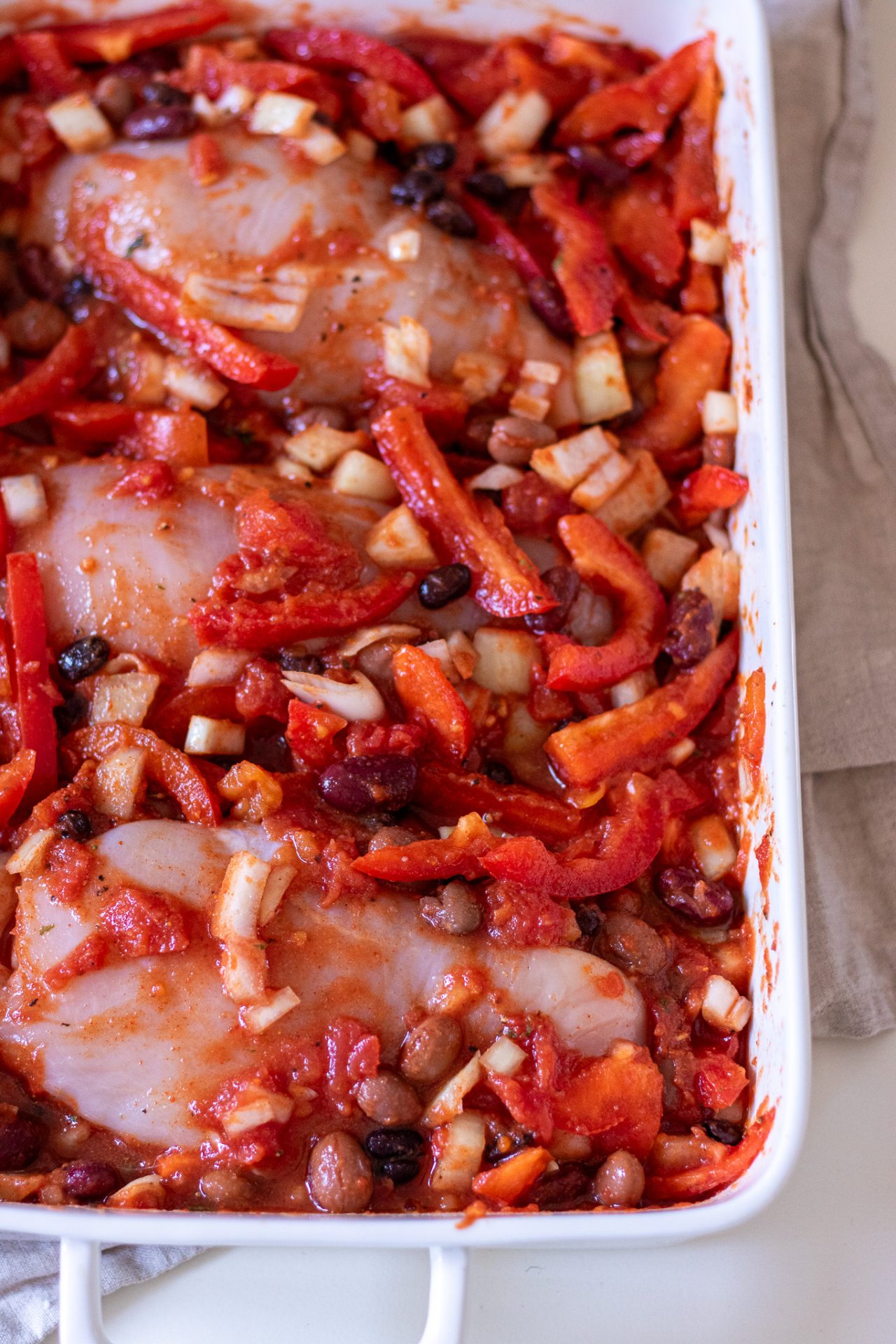 Image of chicken taco bake before it's cooked; chicken breast, vegetables, beans and taco seasoning in a baking dish