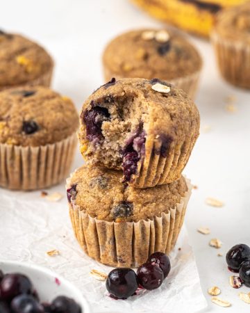 Banana blueberry oat muffins in a stack, showing the juicy baked blueberries inside.