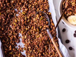 Tray of chocolate olive oil granola with a spoon, small bowl to the side