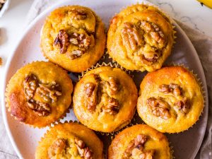 Pumpkin banana and walnut muffins arranged on small white ceramic plate, on top of neutral linen napkin