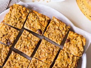 Banana oatmeal bars on a white plate with rolled oats and bananas